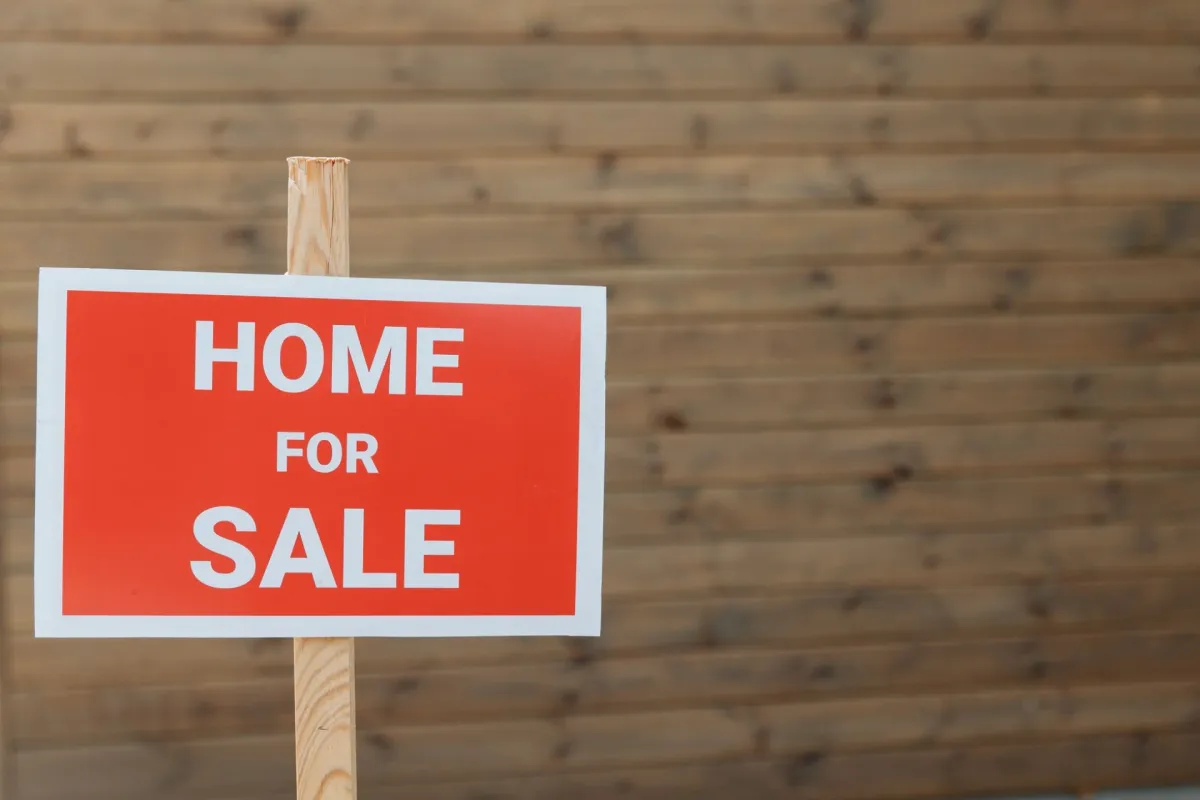 A red home for sale sign against a wooden backdrop.