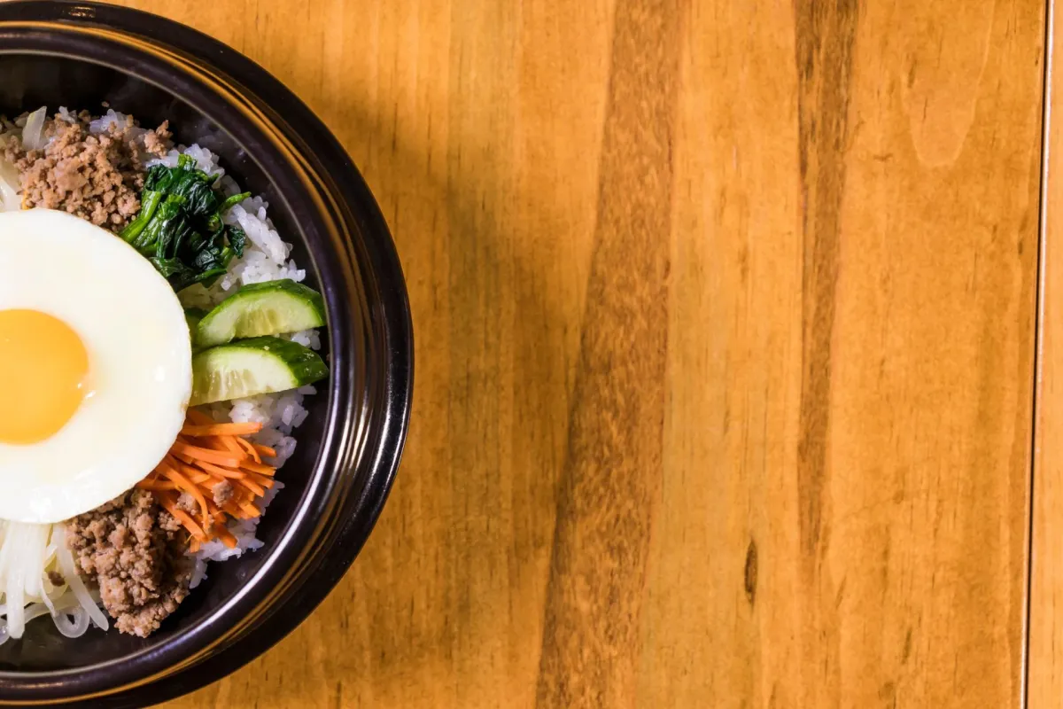 Korean bibimbap with vegetables and egg served in a stone bowl.