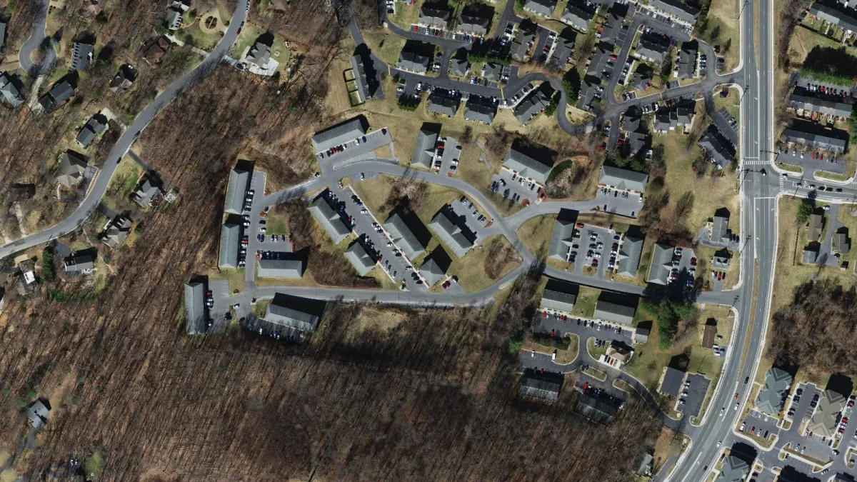 Aerial view of the Hillmont Circle area in southeast Harrisonburg, showing existing apartment buildings, townhouse rows, and wooded land around the site