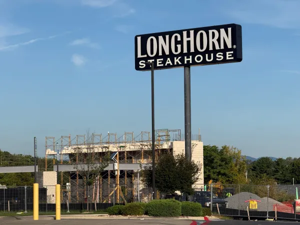 LongHorn Steakhouse sign on Burgess Road in Harrisonburg with the Discount Tire building under construction behind it, scaffolding around block walls