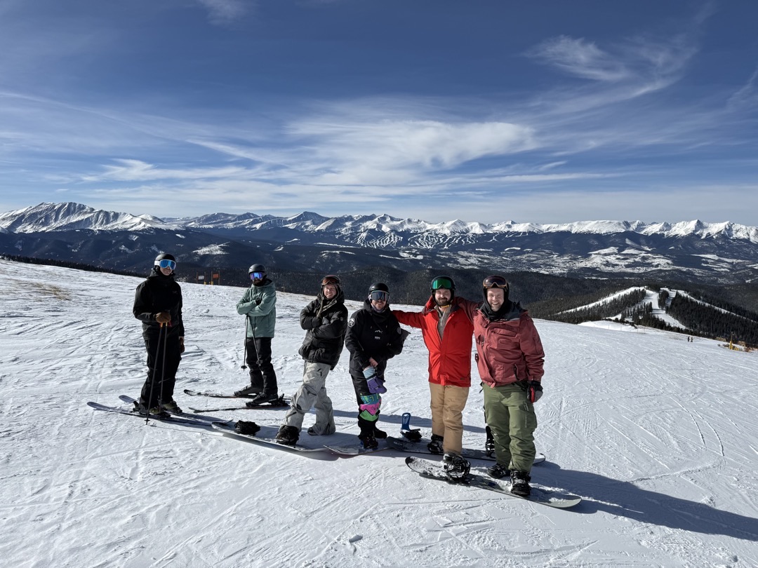 Six friends on skis and snowboards at the top of Keystone with the Rockies behind them